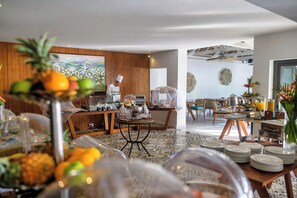 A modern dining area with wooden paneling, a chef at the counter, and a view of a cityscape through a large window. - Seasense Boutique Hotel & Spa (Belle Mare)