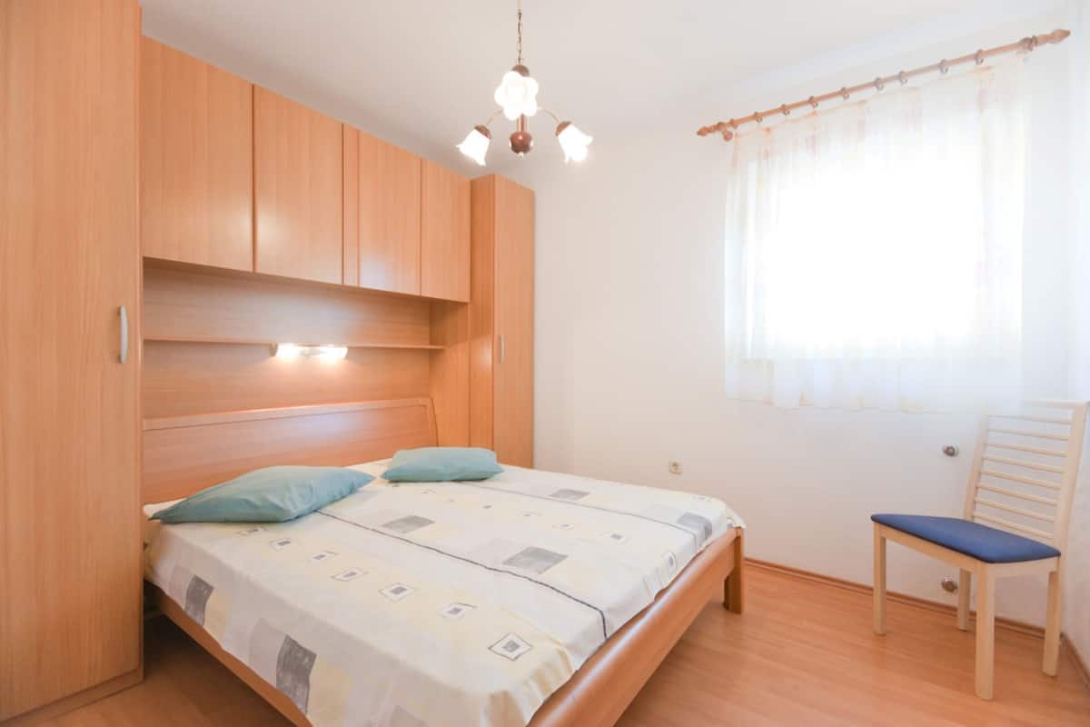 A bedroom with a bed, wooden wardrobe, and a chair.