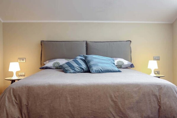 A neatly made bed with a grey headboard, two bedside lamps, and a beige wall. - B&B Portanova (Salerno)
