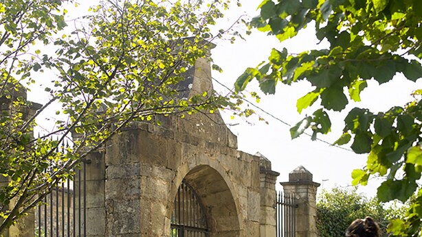 Un arco de piedra que da acceso a un jardín con una banca y una mesa.