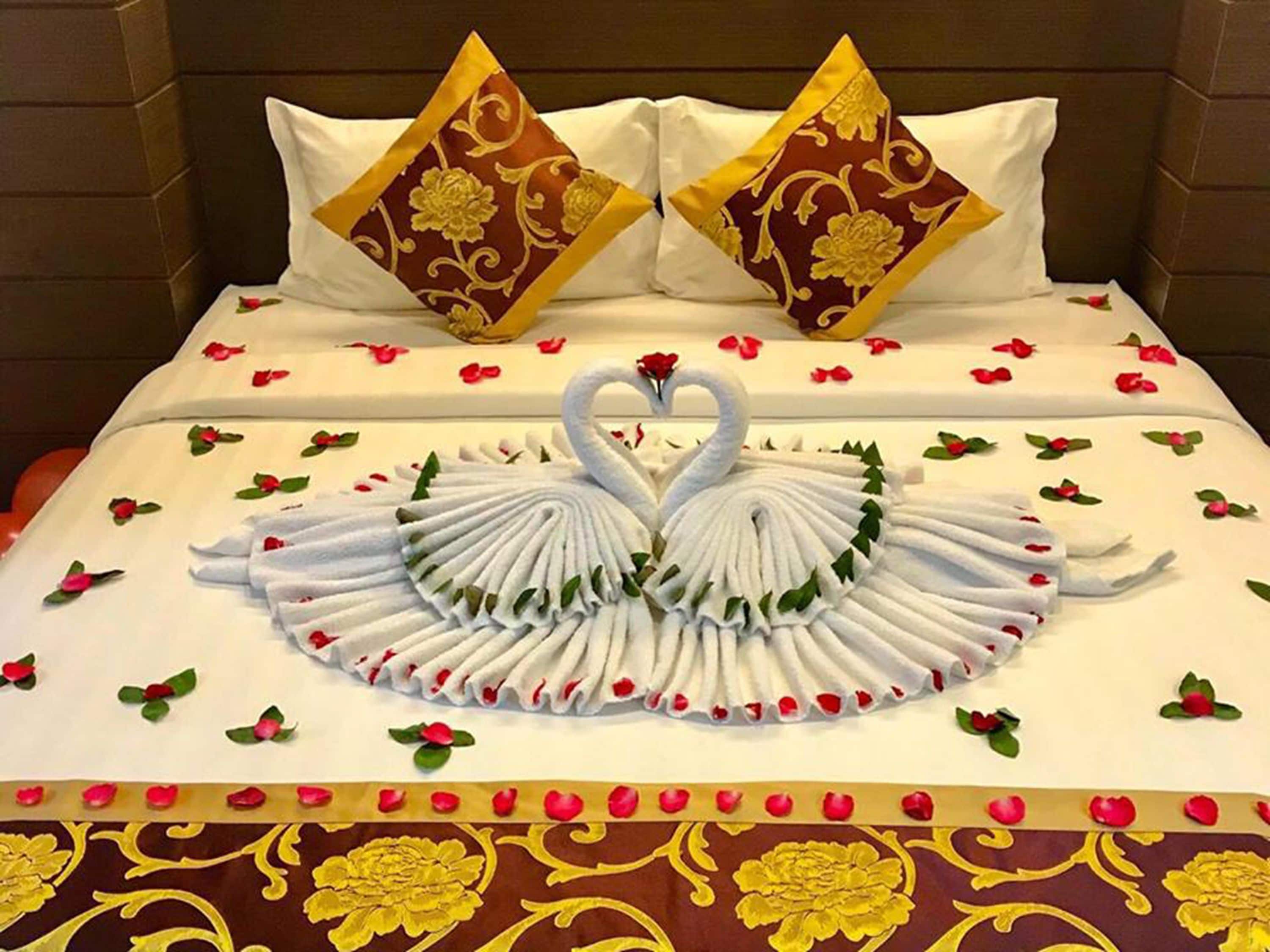A bed with a swan towel art, rose petals, and two decorative pillows.