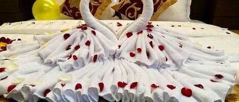 Una cama con una toalla dispuesta en forma de corazón y pétalos de rosa.