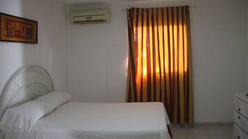 A bedroom with a bed, a headboard, a nightstand, a dresser, a wall-mounted air conditioner, and a curtain.