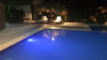 A swimming pool with two white lounge chairs and a thatched umbrella in the background.