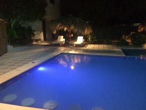 A swimming pool with two white lounge chairs and a thatched umbrella in the background.