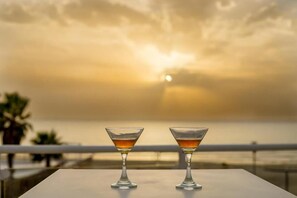 Dos copas de martini sobre una mesa con vista al atardecer.