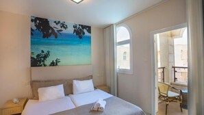Ein Hotelzimmer mit Bett, einem Strandbild, einem Telefon und Blick auf den Balkon.