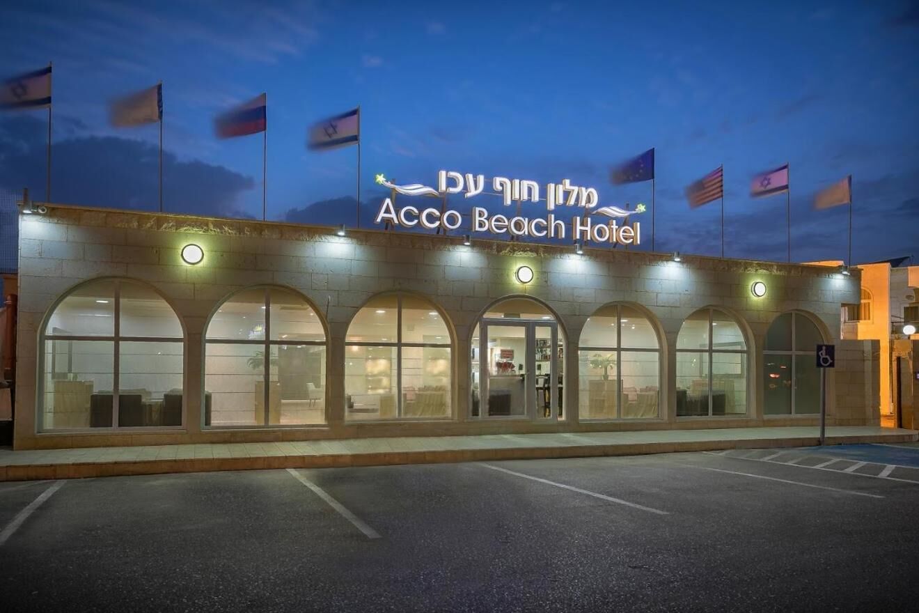 Exterior del Hotel Acco Beach, con ventanas arqueadas y banderas.