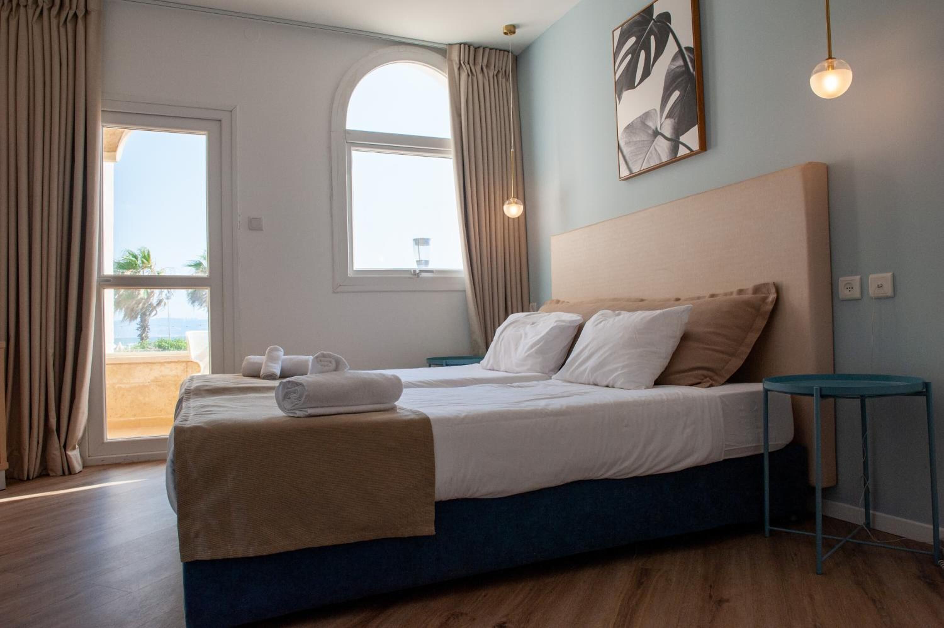 A bedroom with a bed, a bedside table, a window with curtains, and a view of the outdoors.