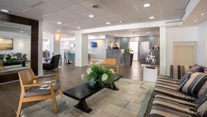 Eine moderne Lobby mit einer Rezeption, einer Sitzecke und einem großen Spiegel.