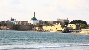 Eine Küstenstadtansicht mit einer markanten Moschee, die eine grüne Kuppel und einen Minarett besitzt, neben einer befestigten Mauer.