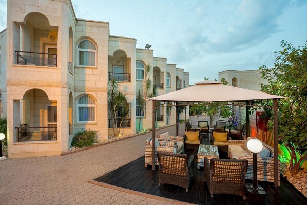 Un patio con mobiliario exterior, una pérgola y un edificio con ventanas de arco y balcones.