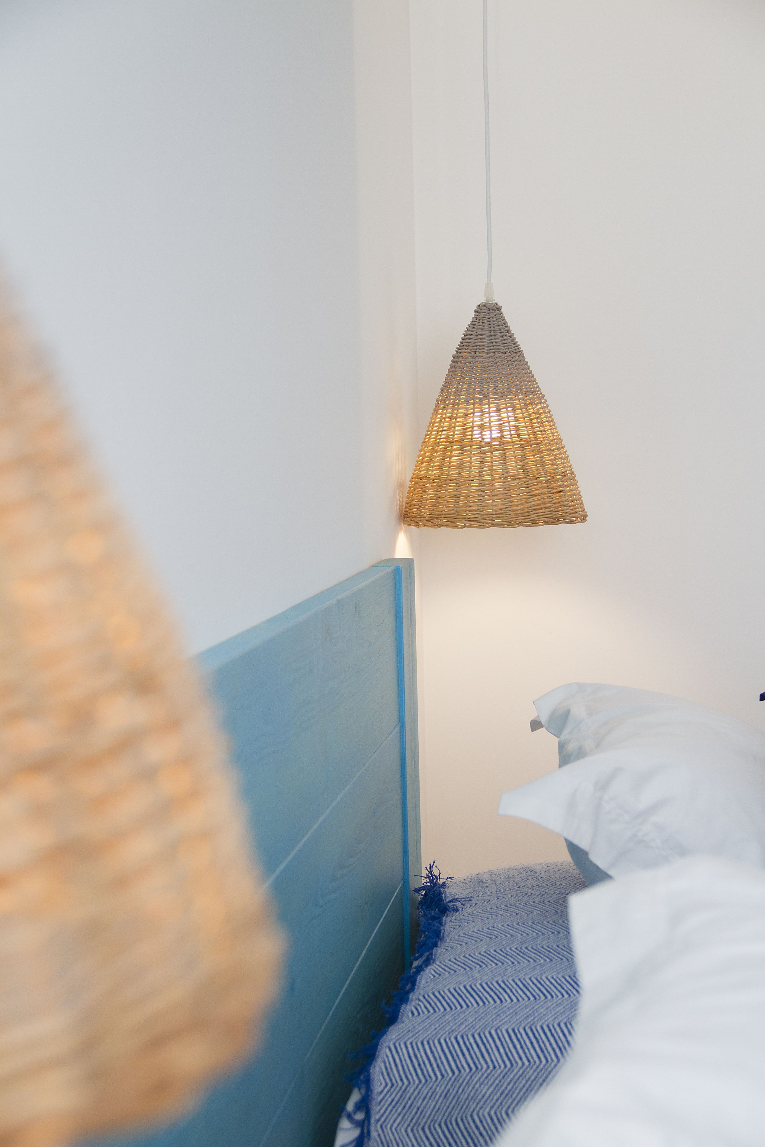 Een slaapkamer met een bed, een blauw hoofdbord en een geweven hanglamp.
