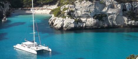 A white sailboat anchored near a rocky coastline with clear turquoise water.