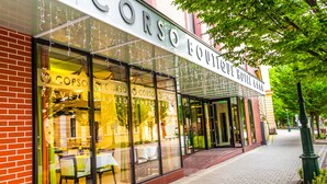A hotel with a glass facade, outdoor seating, and a brick exterior. - Corso Boutique Hotel (Gyula)