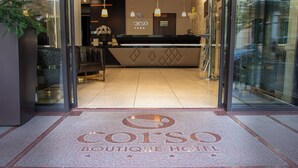 A hotel entrance with a reception desk, a sign reading "CORSO Boutique Hotel," and a decorative doormat. - Corso Boutique Hotel (Gyula)