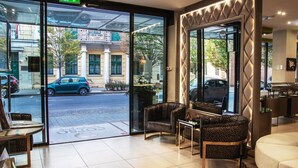 A hotel lobby with glass doors, seating area, and a view of the street outside. - Corso Boutique Hotel (Gyula)
