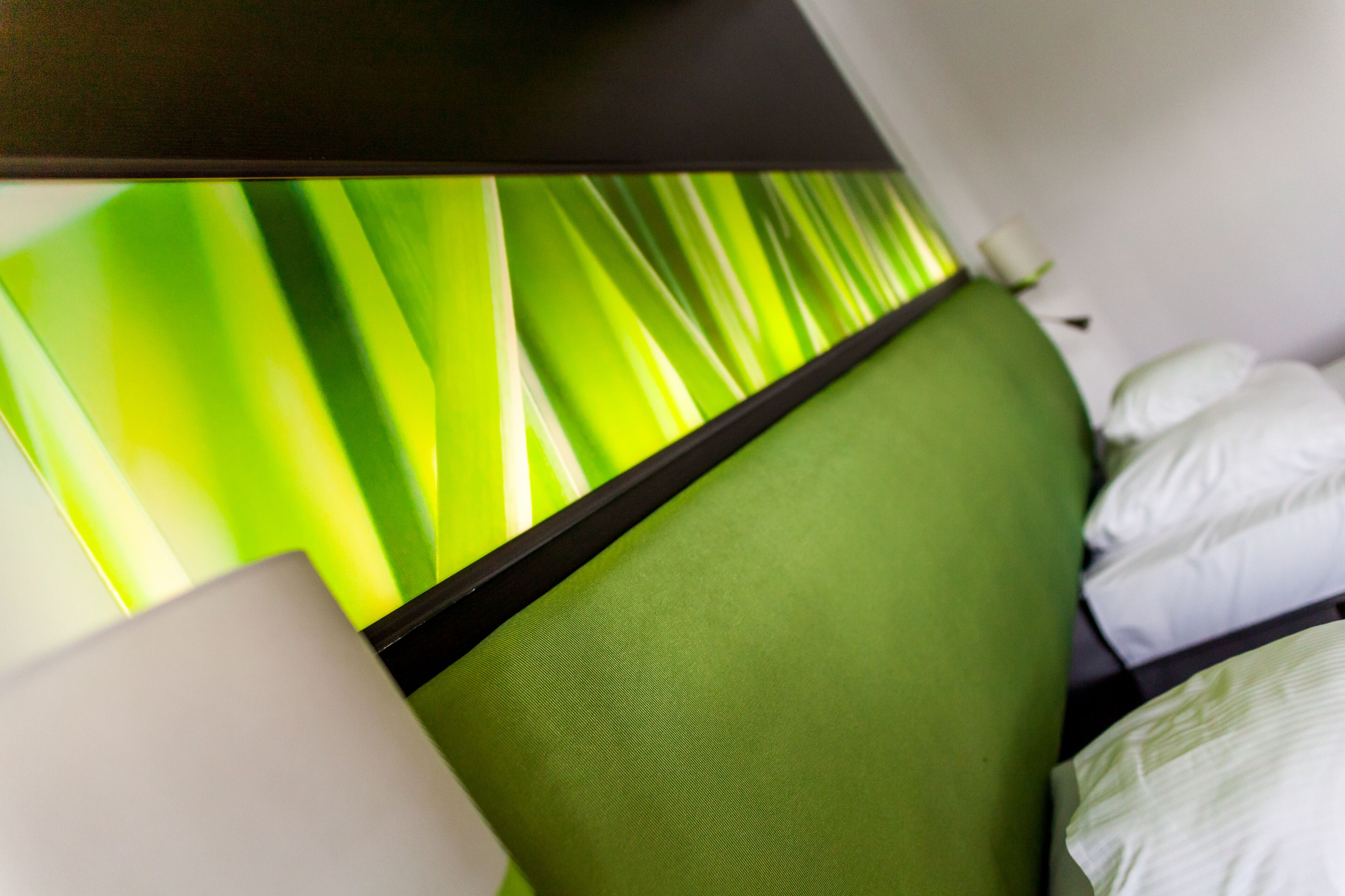 Une chambre avec une tête de lit verte, des oreillers blancs et une fenêtre avec des stores verts.