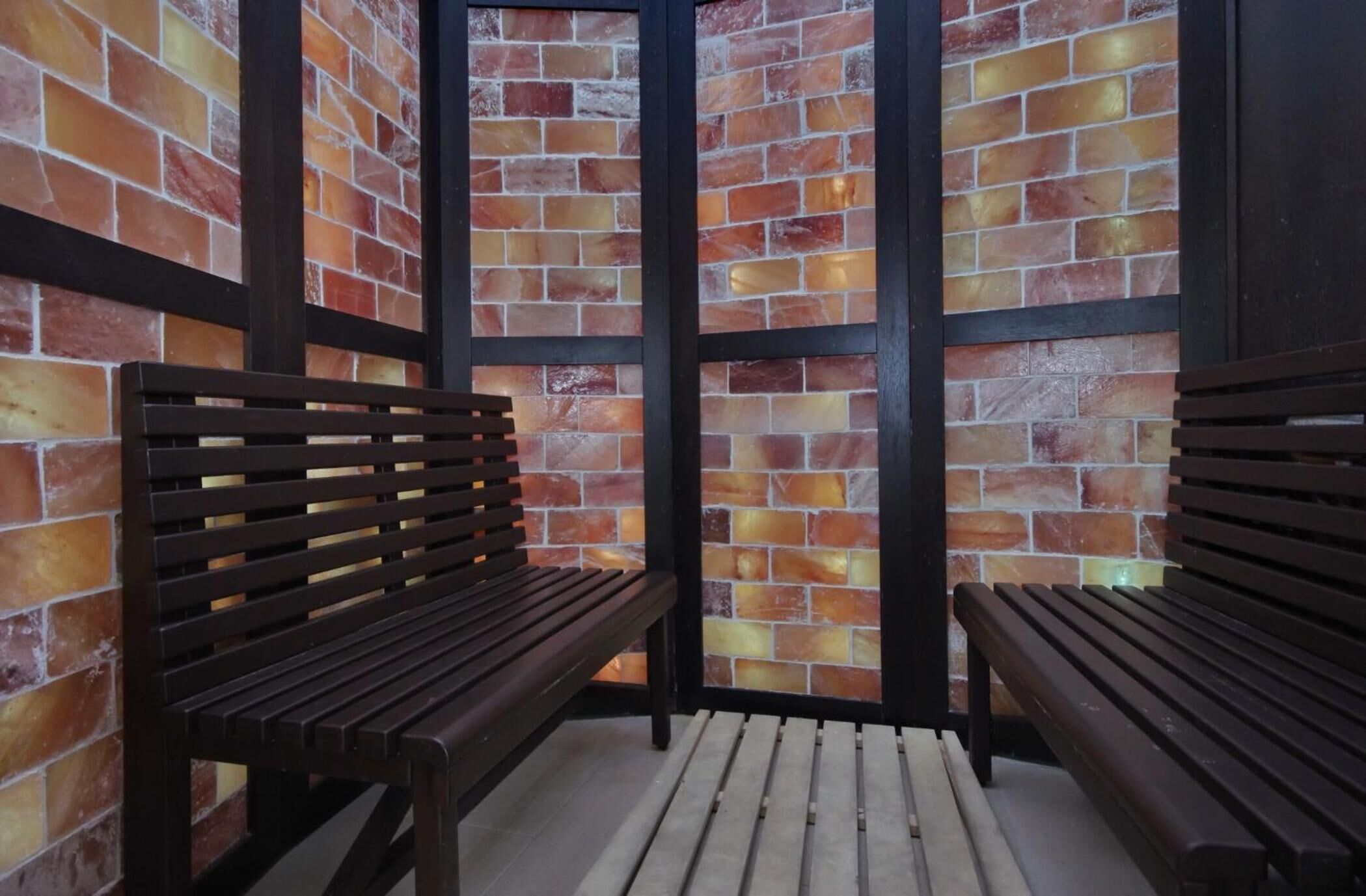 A covered outdoor seating area with wooden benches and a brick wall backdrop.