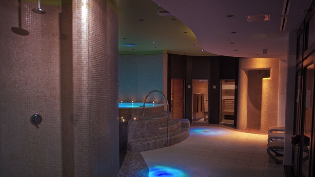 A spa area with a hot tub, tiled walls, and a seating area with benches. - Corso Boutique Hotel (Gyula)