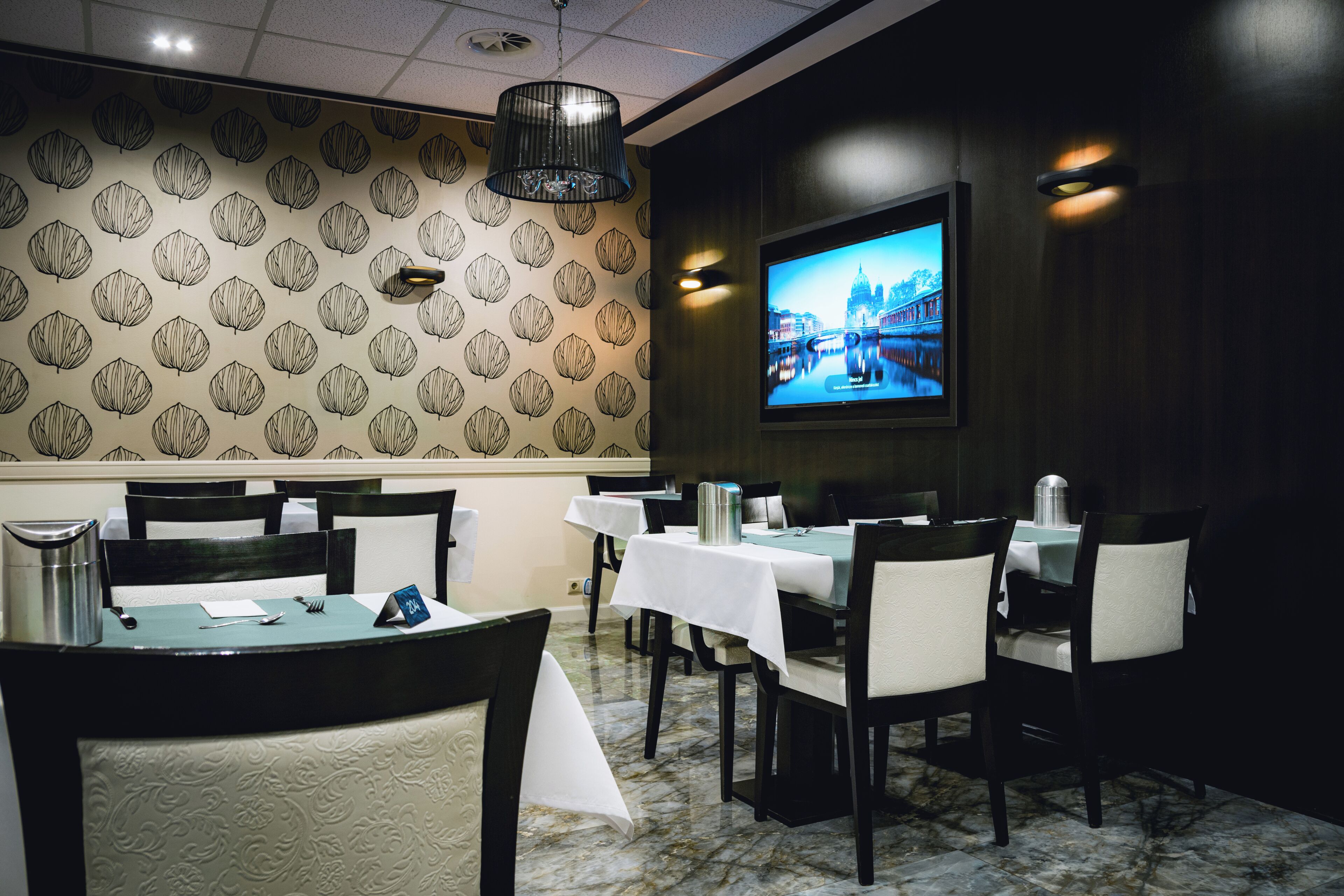 Un ristorante con un muro decorato, uno schermo televisivo e tavoli apparecchiati per la cena.