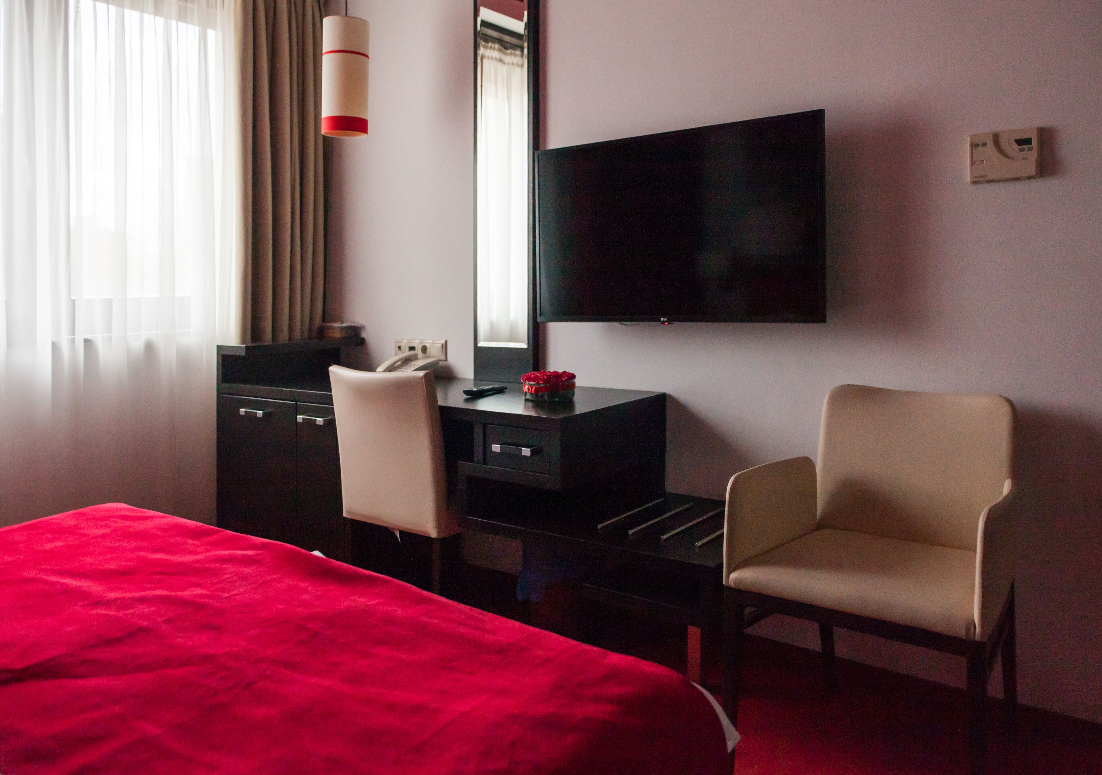 Une chambre d’hôtel avec un lit, un bureau et une chaise, une télévision et une fenêtre avec des rideaux.