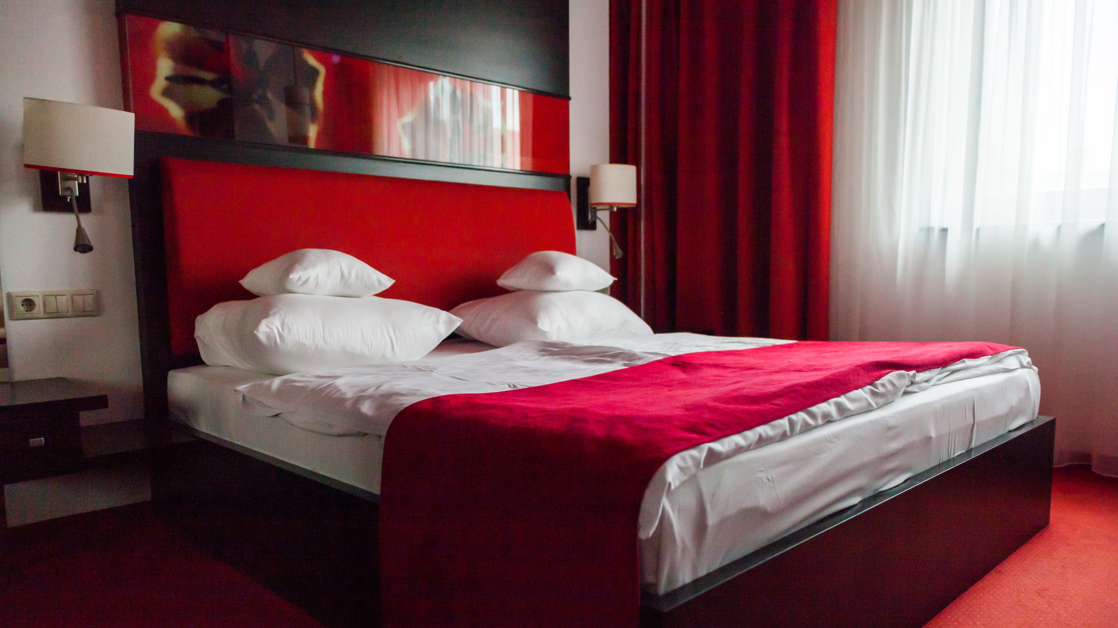 A hotel room with a large bed, red curtains, and a red headboard.
