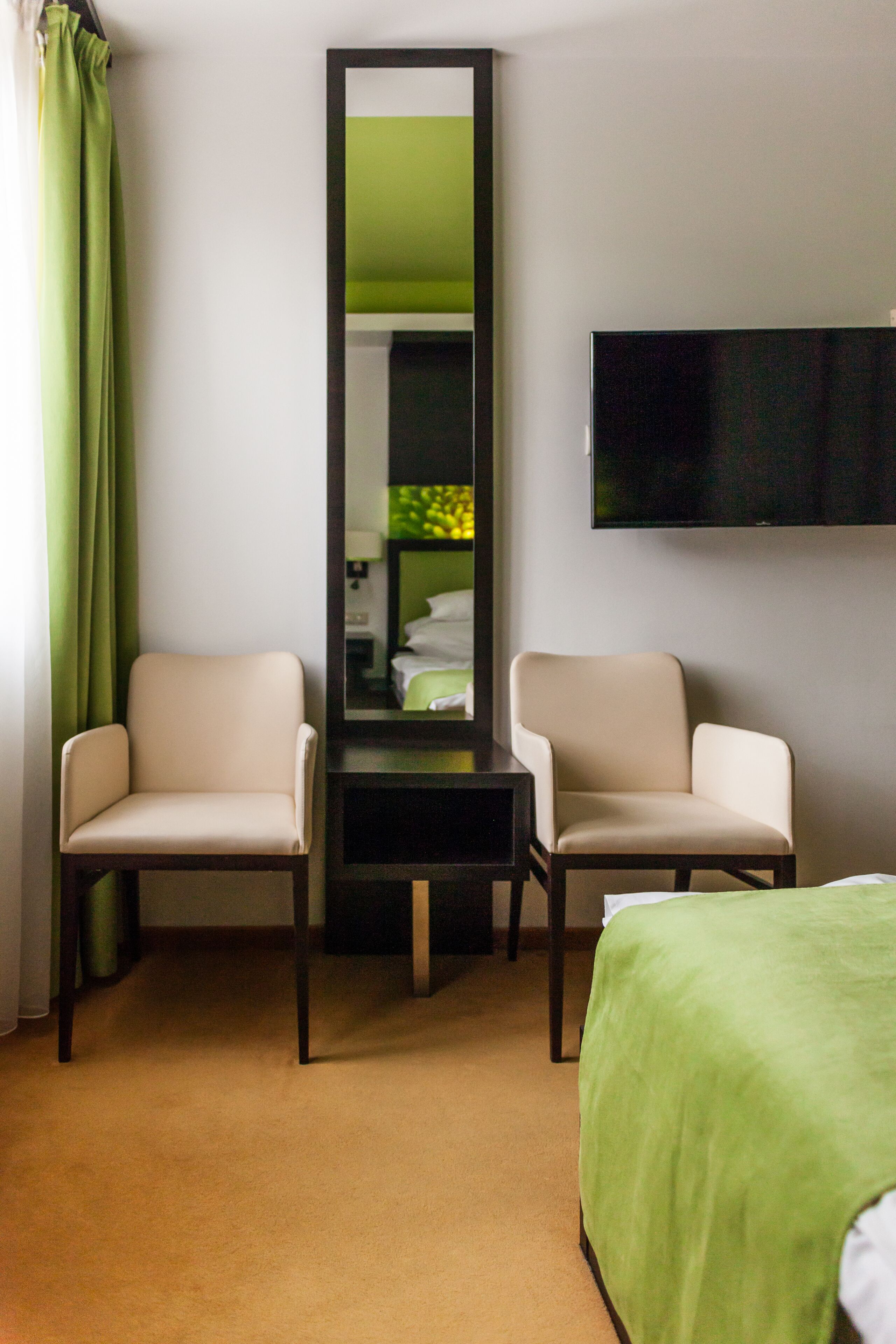 A hotel room with two chairs, a bed, a flat-screen TV, and a mirror.