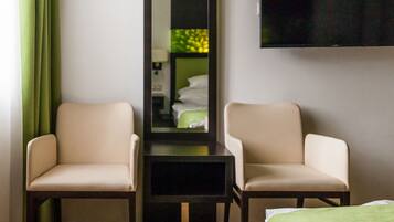 A hotel room with two chairs, a bed, a flat-screen TV, and a mirror.