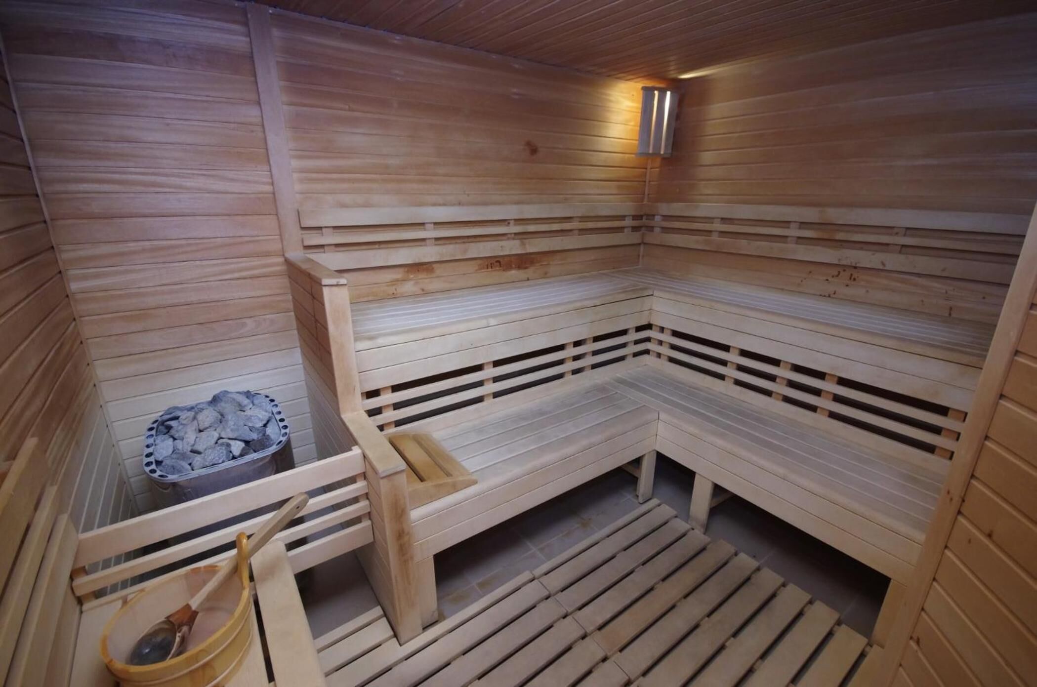 A sauna with wooden benches, a bench with a small tray, and a container of stones.