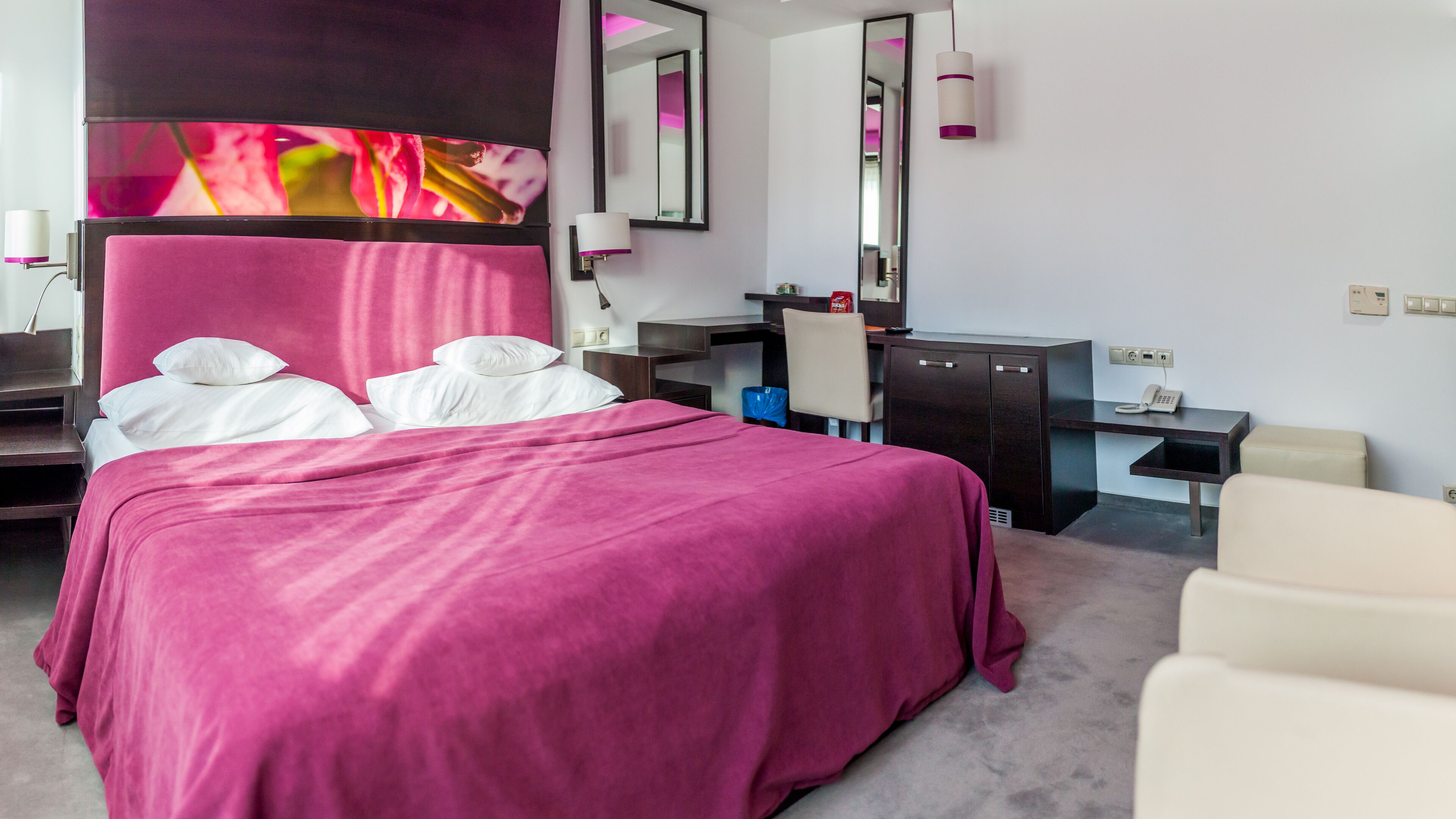 A hotel room with a large bed, a desk, a chair, a mirror, and a television.