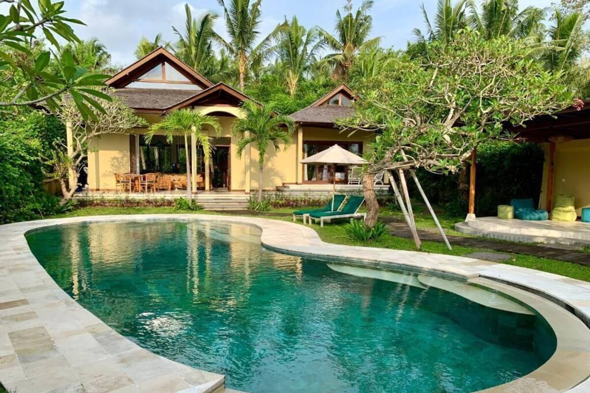 A pool area with a curved edge, surrounded by palm trees and a building with a sloped roof.