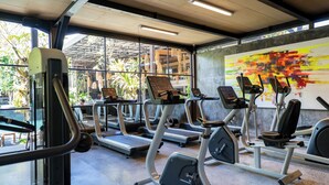 A gym with treadmills, elliptical machines, and a large window with a view of palm trees. - Surya Kembar Villas (Ubud)
