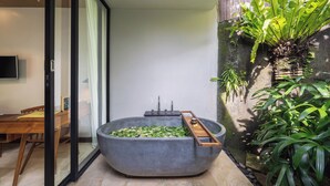 A modern bathroom with a large bathtub, a wooden bench, and a potted plant. - Surya Kembar Villas (Ubud)