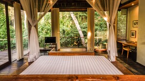 A spacious bedroom with a large bed, wooden flooring, and a balcony with a view of lush greenery. - Surya Kembar Villas (Ubud)
