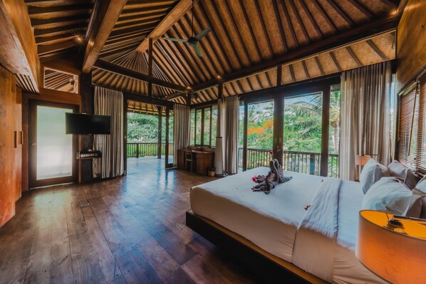 A spacious bedroom with a large bed, a television, and a balcony with a view of greenery.
