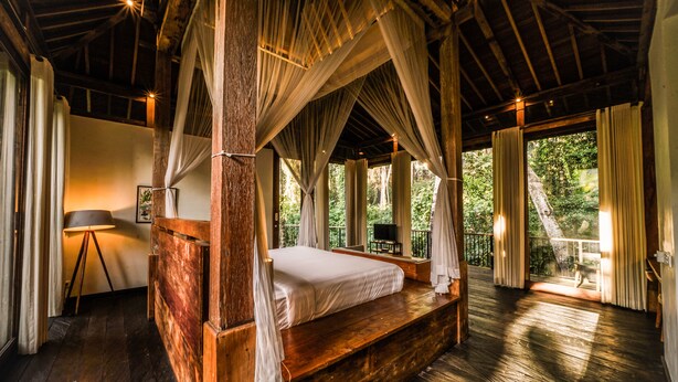 A four-poster bed with a canopy, a lamp, and a view of the outdoors. - Surya Kembar Villas (Ubud)