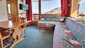 A cozy cabin interior with a wooden table, chairs, a sofa, and a TV.