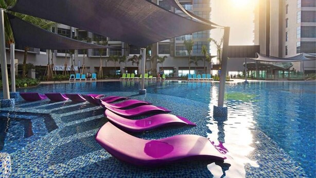 A swimming pool with floating exercise mats, a shaded area, and high-rise buildings in the background. - Damai at Atlantis Residences Melaka (Malacca City)