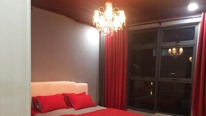 A bedroom with a large bed, red curtains, a chandelier, and a view through a window. - Damai at Atlantis Residences Melaka (Malacca City)