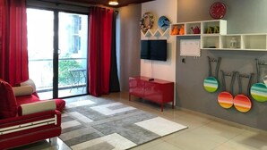 A living room with a red sofa, a TV, a red cabinet, and a wall with decorative items and a clock. - Damai at Atlantis Residences Melaka (Malacca City)