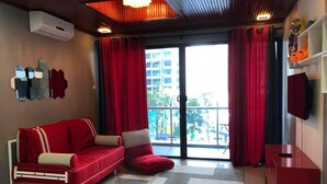 A modern living room with a red sofa, a red ottoman, a TV on the wall, and a balcony with red curtains. - Damai at Atlantis Residences Melaka (Malacca City)