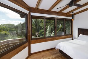 Une chambre dotée d’une grande fenêtre, de poutres apparentes en bois au plafond et d’un ventilateur de plafond.