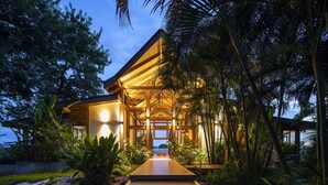 A modern house with a wooden deck leading to a covered entrance, surrounded by tropical vegetation. - Luxury Villa Melody- Santa Teresa beach  (Playa Santa Teresa)