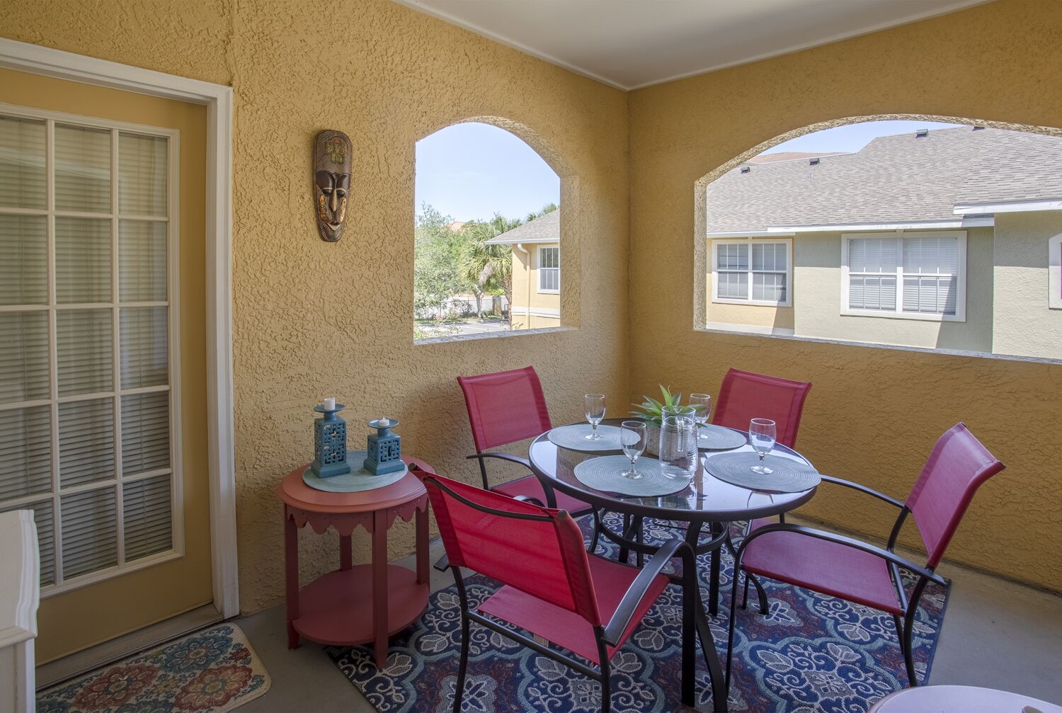A sunlit patio with a round table, red chairs, and a small side table with candles.