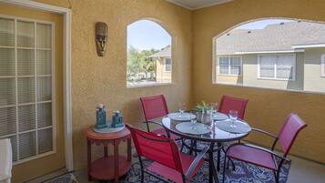 A sunlit patio with a round table, red chairs, and a small side table with candles.