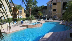 A swimming pool with lounge chairs and a small hot tub, surrounded by palm trees and a multi-story building. - PROMO PRICES!!CLEARWATER BEACH 2beds,2baths,FREE WI-FI/Parking in gated comunity (Clearwater)