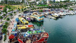 A marina with multiple boats, including a red boat named "The Tropics Boat," and a large building in the background. - PROMO PRICES!!CLEARWATER BEACH 2beds,2baths,FREE WI-FI/Parking in gated comunity (Clearwater)