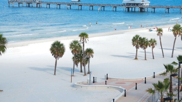 A beach with a pier extending into the ocean, palm trees, and a sandy walkway. - PROMO PRICES!!CLEARWATER BEACH 2beds,2baths,FREE WI-FI/Parking in gated comunity (Clearwater)
