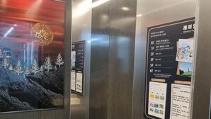 An elevator interior with stainless steel walls, a digital display with floor information, and a security camera.